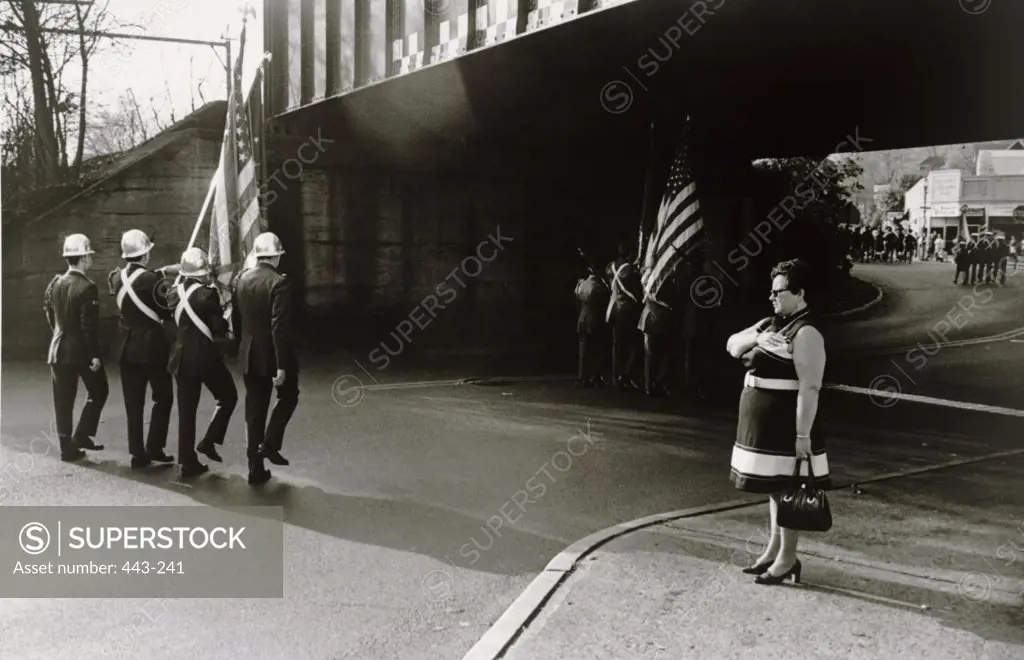 Military men marching on a road with an American flag