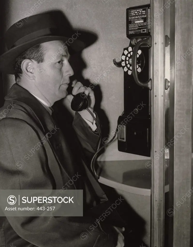 Side profile of a mature man talking on a pay phone, 1954