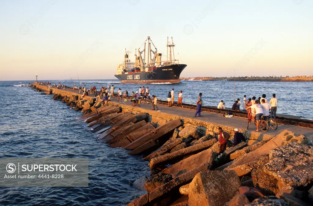 Fishing from North Pier. In the Backround is a container ship about to berth at the harbour. Durban. KwaZulu-Natal. South Africa.