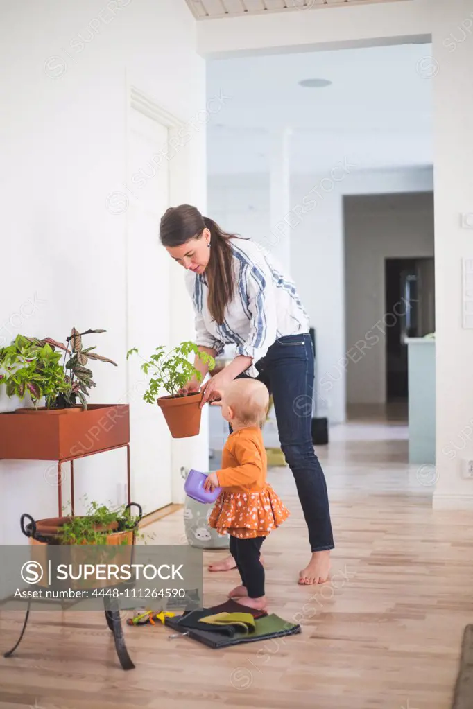 Fashion designer and daughter gardening while standing on hardwood floor at home