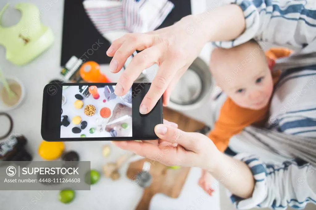 High angle view of female influencer food blogging with baby girl in kitchen