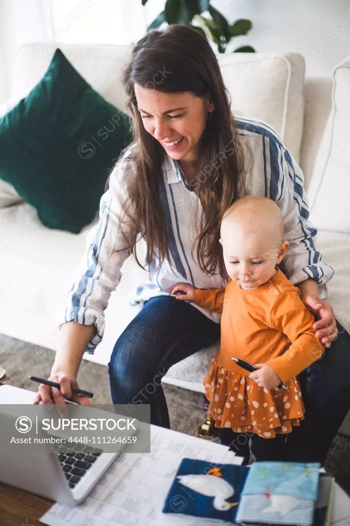 High angle view of smiling businesswoman telecommuting while sitting by daughter on sofa in living room