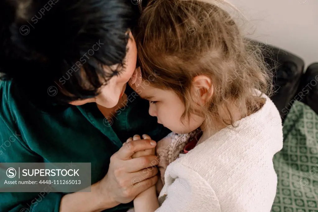 High angle view of mother holding sad daughter while sitting at home