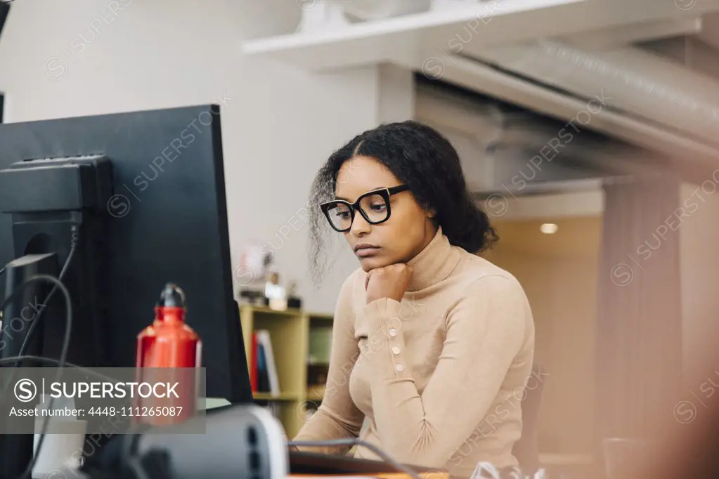 Focused female computer programmer working on laptop at desk in office