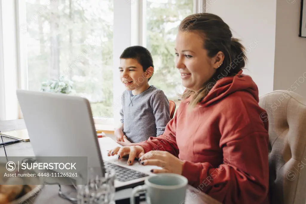 Mother using laptop on table while sitting with autistic son at home