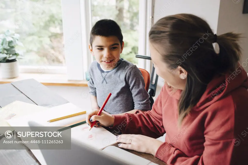 Mother teaching drawing to autistic son while sitting at home