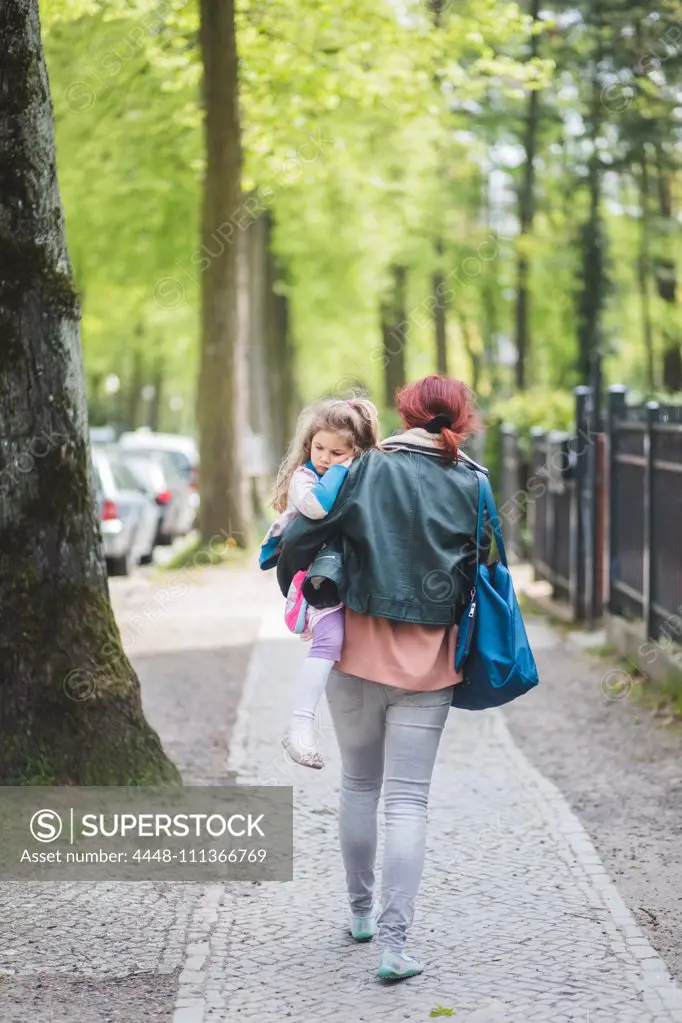 Rear view of mother carrying daughter while walking on footpath