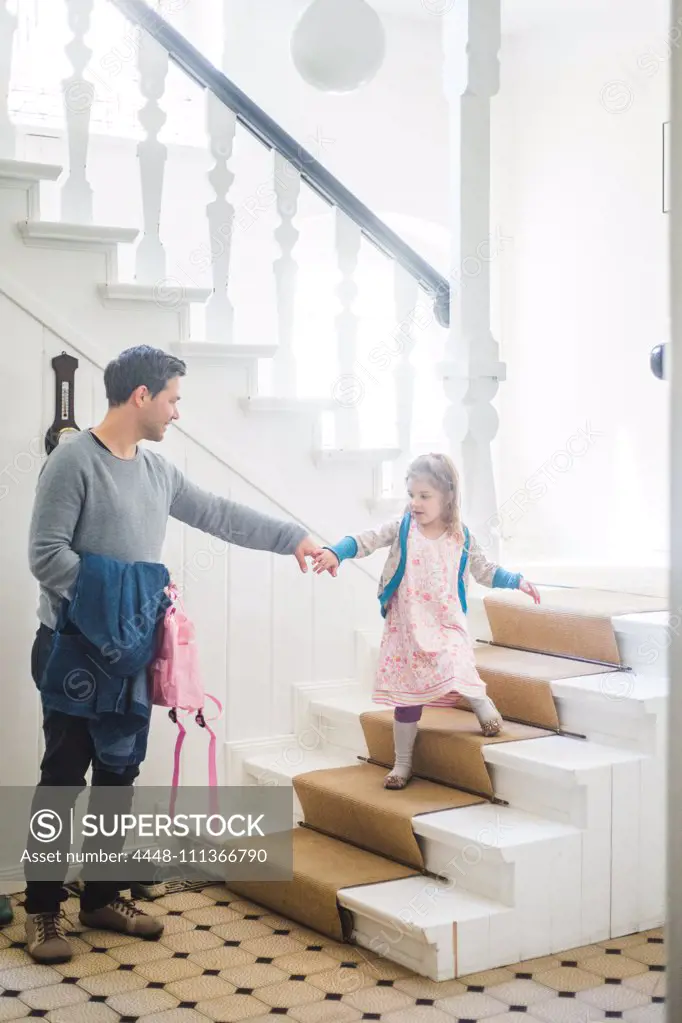 Full length of father holding schoolgirl moving down steps at home