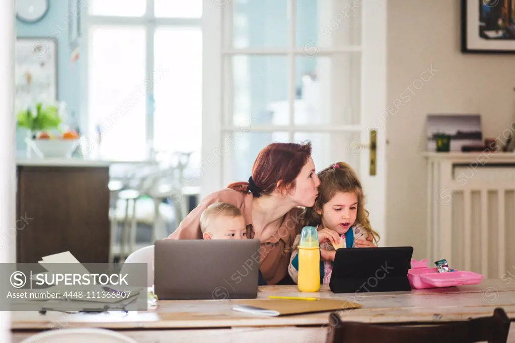 Mid adult woman kissing daughter while sitting with son at home