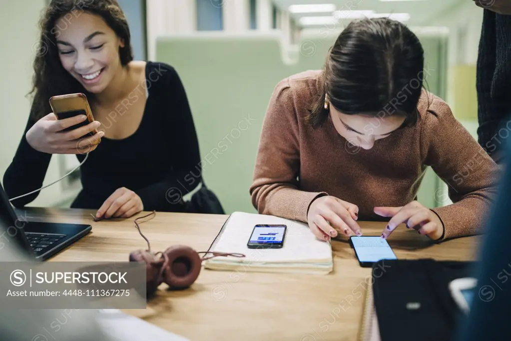 Female high school students using smart phone at desk in classroom