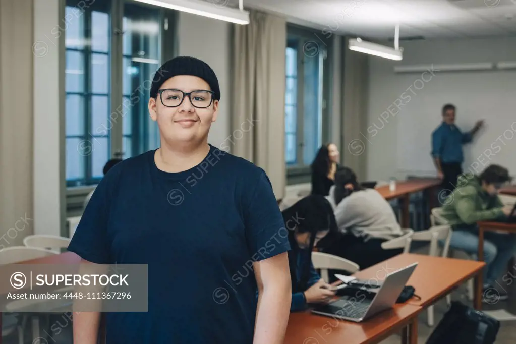 Portrait of teenage boy with classmates at desk in classroom