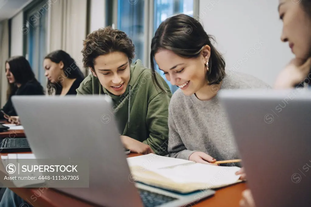 Smiling teenage students studying at desk in school