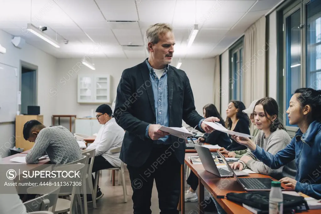 Teacher giving questionnaire to students sitting at desk in classroom