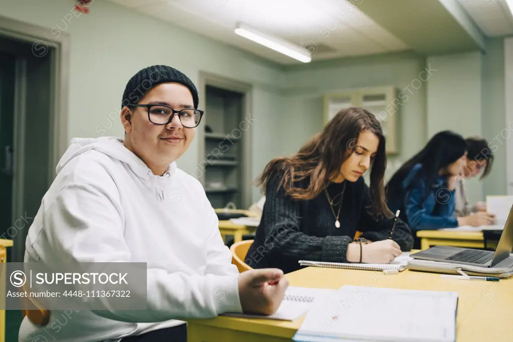 Portrait of smiling male high school student sitting by classmate in classroom