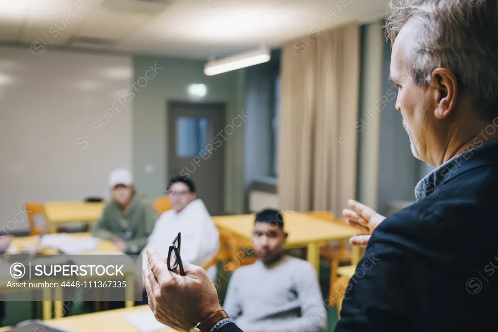 Male teacher gesturing while teaching students in classroom