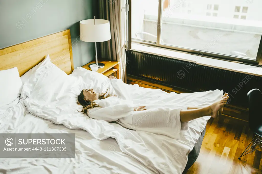 Smiling woman in bathrobe having fun on bed at hotel room