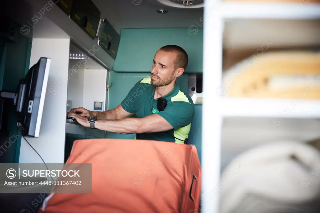 Male paramedic typing while looking at monitoring screen in ambulance