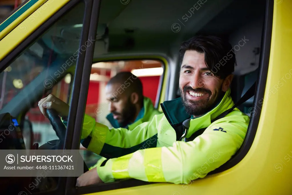 Portrait of smiling male paramedic with coworker driving ambulance in parking lot