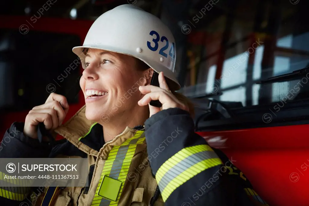 Smiling female firefighter wearing helmet at fire station