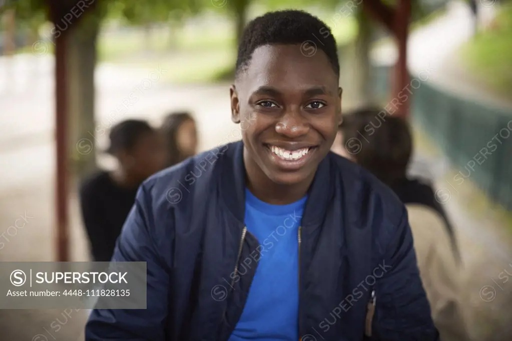 Portrait of smiling teenage boy sitting at park