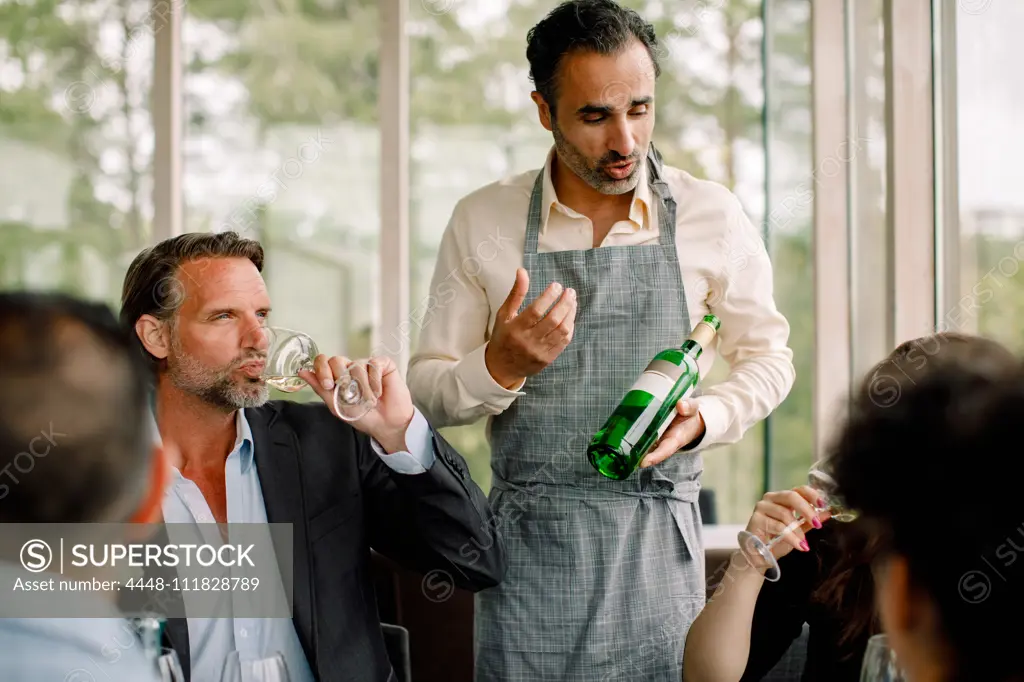 Businessman with wine bottle explaining colleagues at convention center