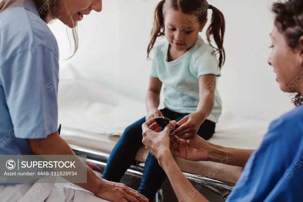 Healthcare worker showing glaucometer to girl by doctor in clinic