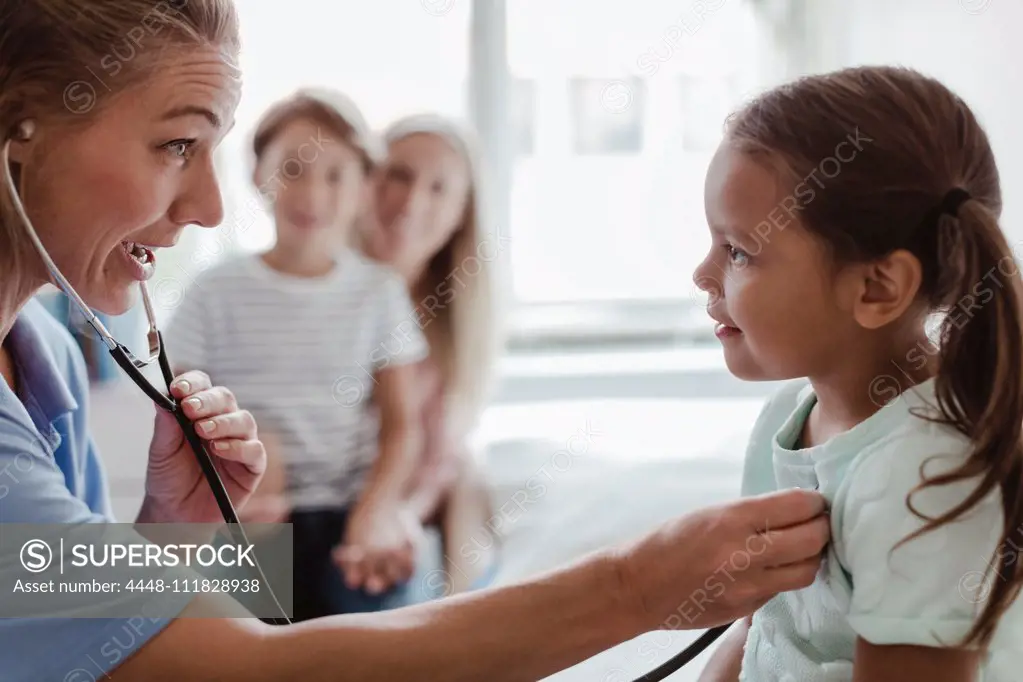 Female pediatrician listening to girl's heartbeat through stethoscope at clinic