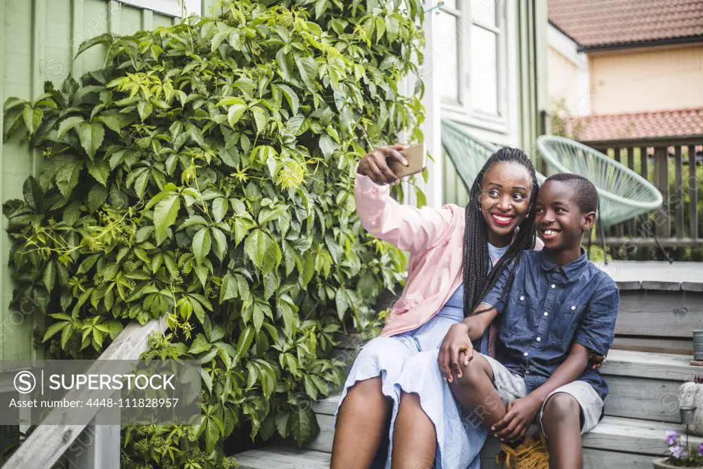 Mother taking selfie through smart phone while sitting by plants on steps