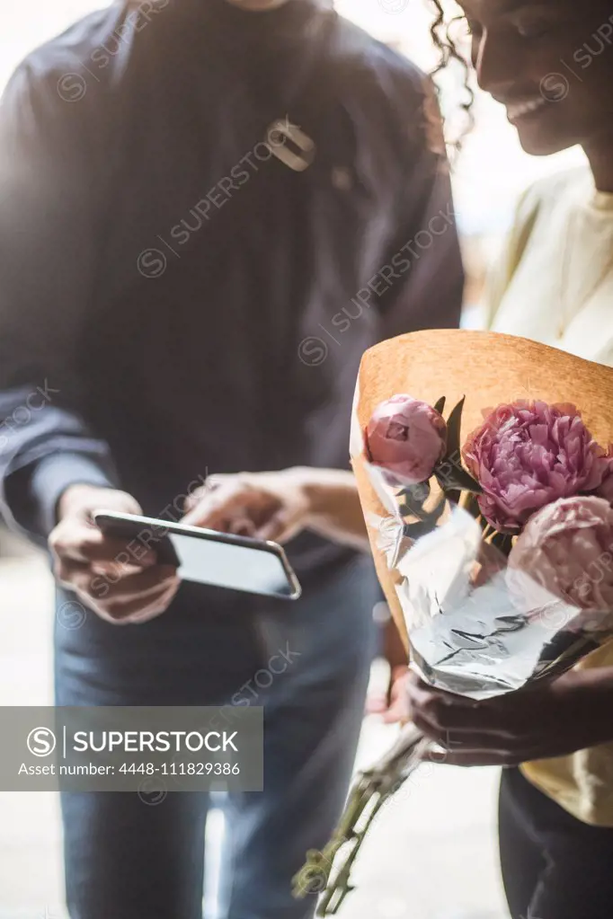 Midsection of delivery man taking sign from female customer while delivering bouquet