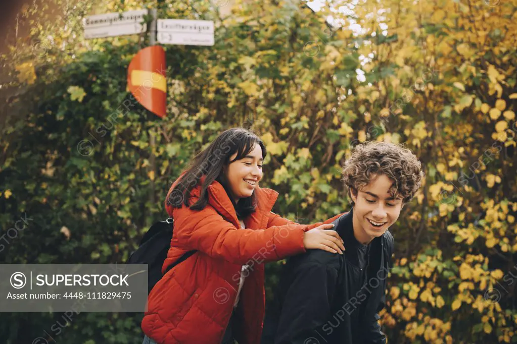 Male and female teenage friends enjoying against trees during autumn