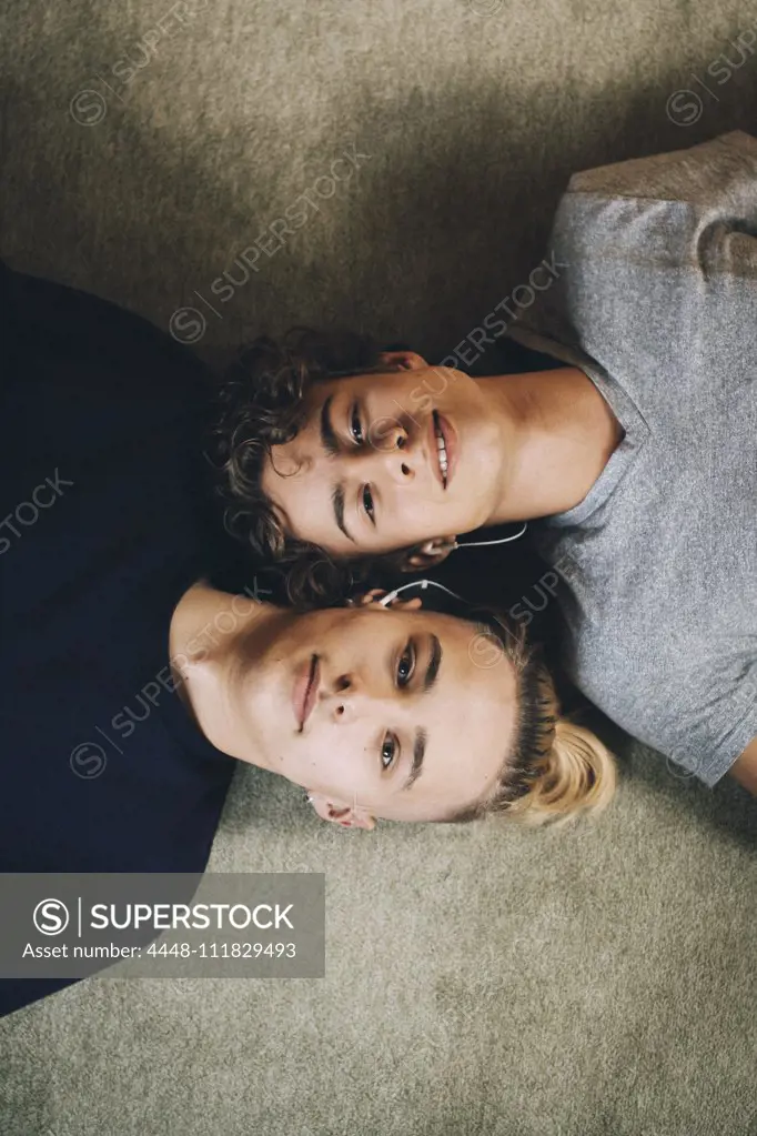 Directly above portrait of teenage boys lying together on carpet at home