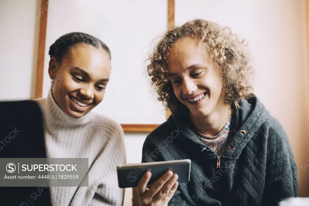 Male and female teenagers smiling while looking at smart phone in room