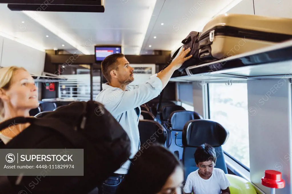 Mid adult man arranging suitcase on shelf in train during family trip