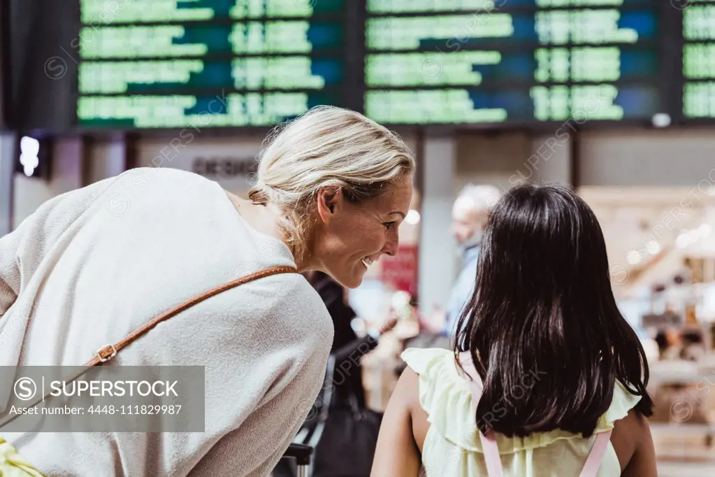 Rear view of smiling mother talking to daughter at railroad station