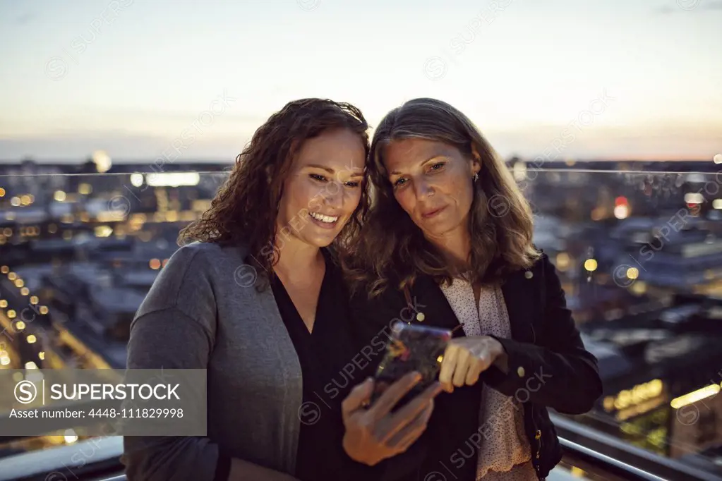 Businesswomen taking selfie on smart phone while standing on terrace after work