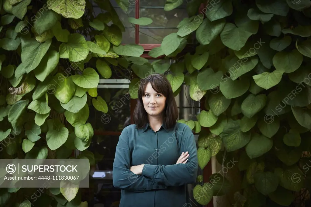 Portrait of confident female architect standing against creeper plants in backyard