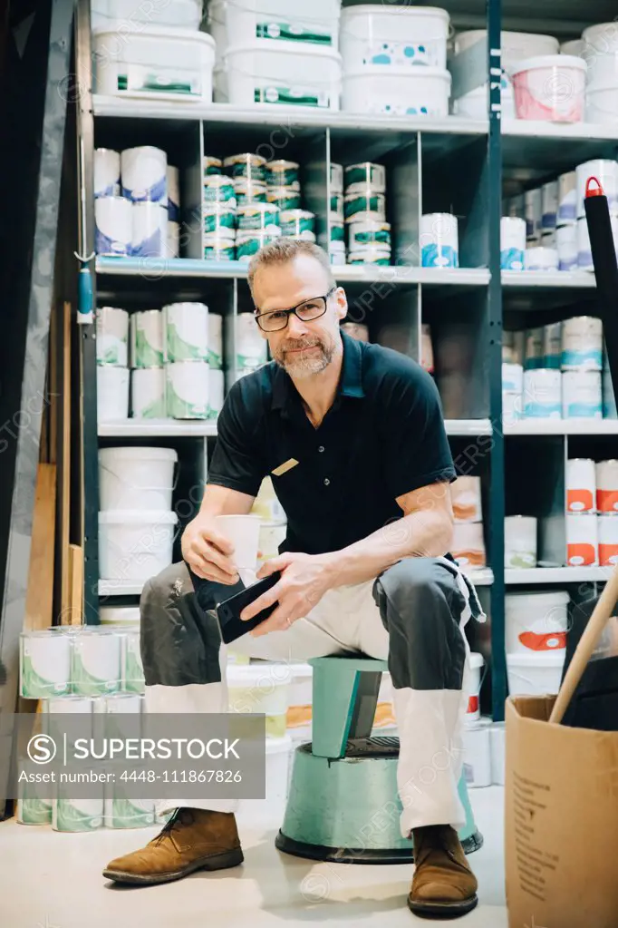 Full length of portrait of salesman sitting on stool in storage room