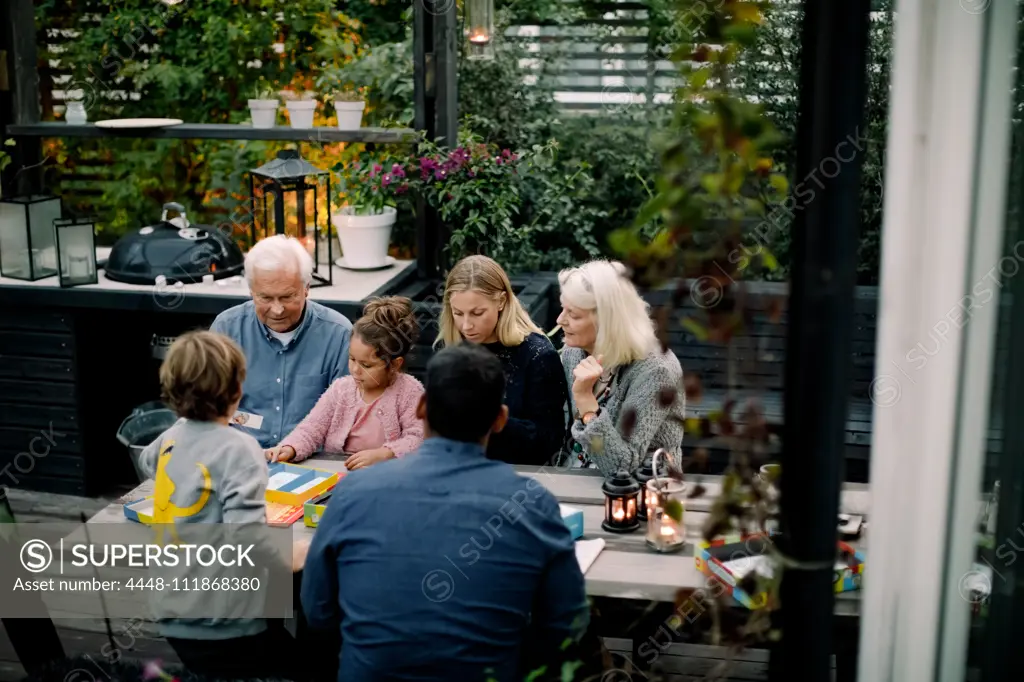 High angle view of family playing board game on table while sitting in patio