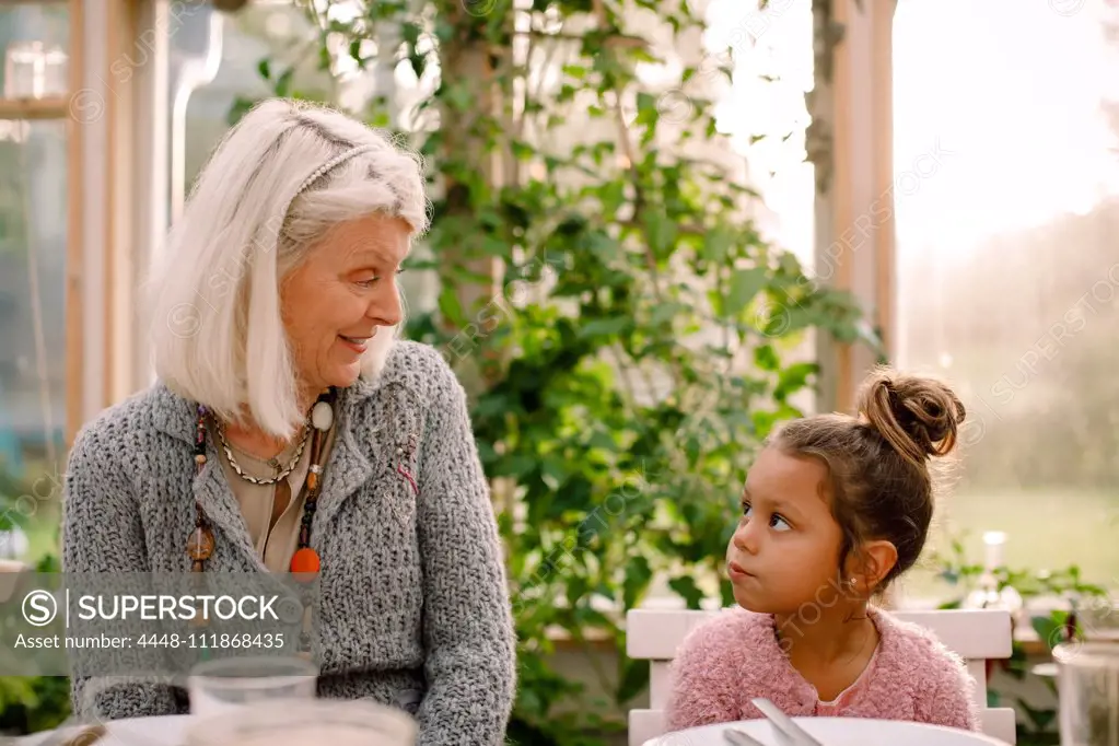 Smiling grandmother looking at granddaughter while having lunch