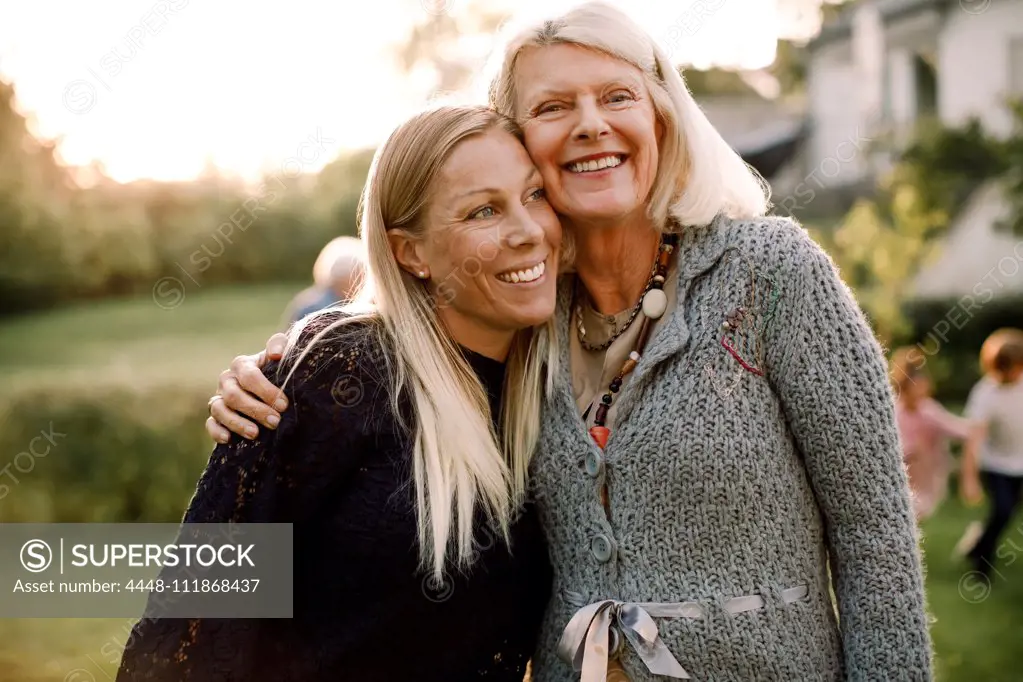 Smiling senior woman and daughter standing with arm around in backyard