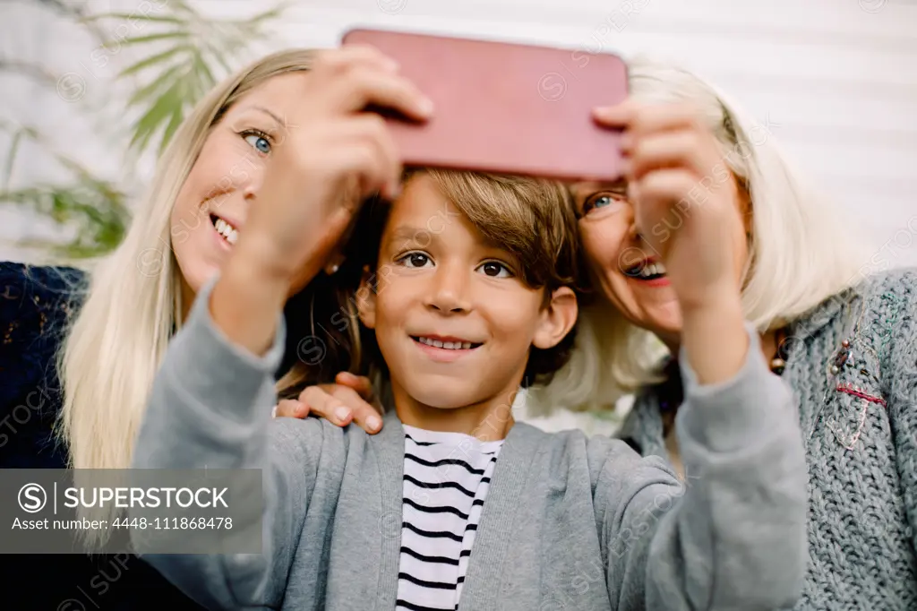 Smiling boy taking selfie with mother and grandmother in mobile phone