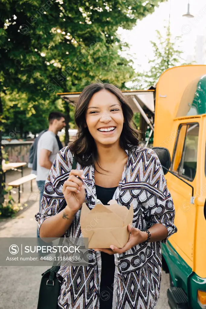 Female customer laughing while standing with box near food truck