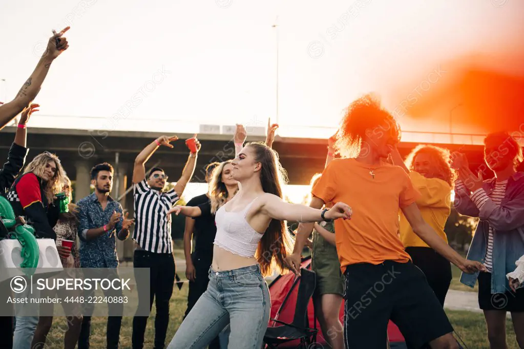 Happy men and women looking at friends dancing in musical event against sky