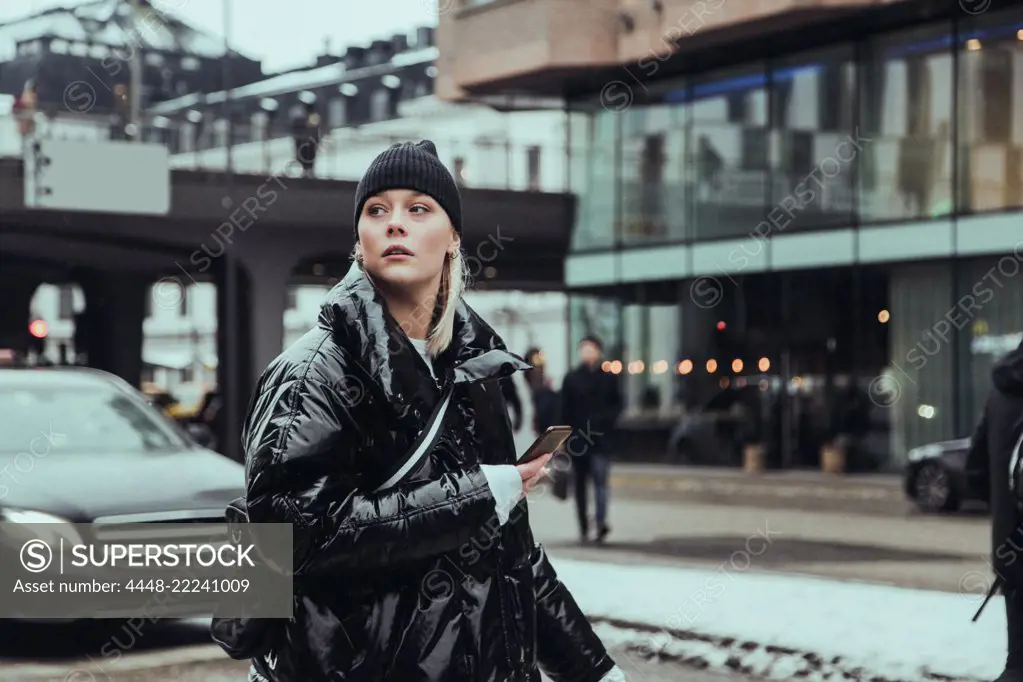 Young woman wearing warm clothing while looking away on street in city during winter