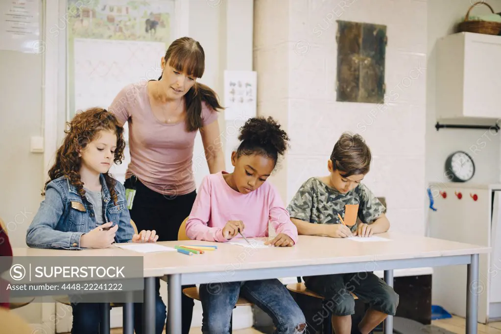 Teacher looking at students writing at desk in elementary classroom