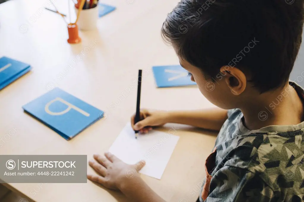 High angle view of schoolboy practicing alphabets at table in classroom