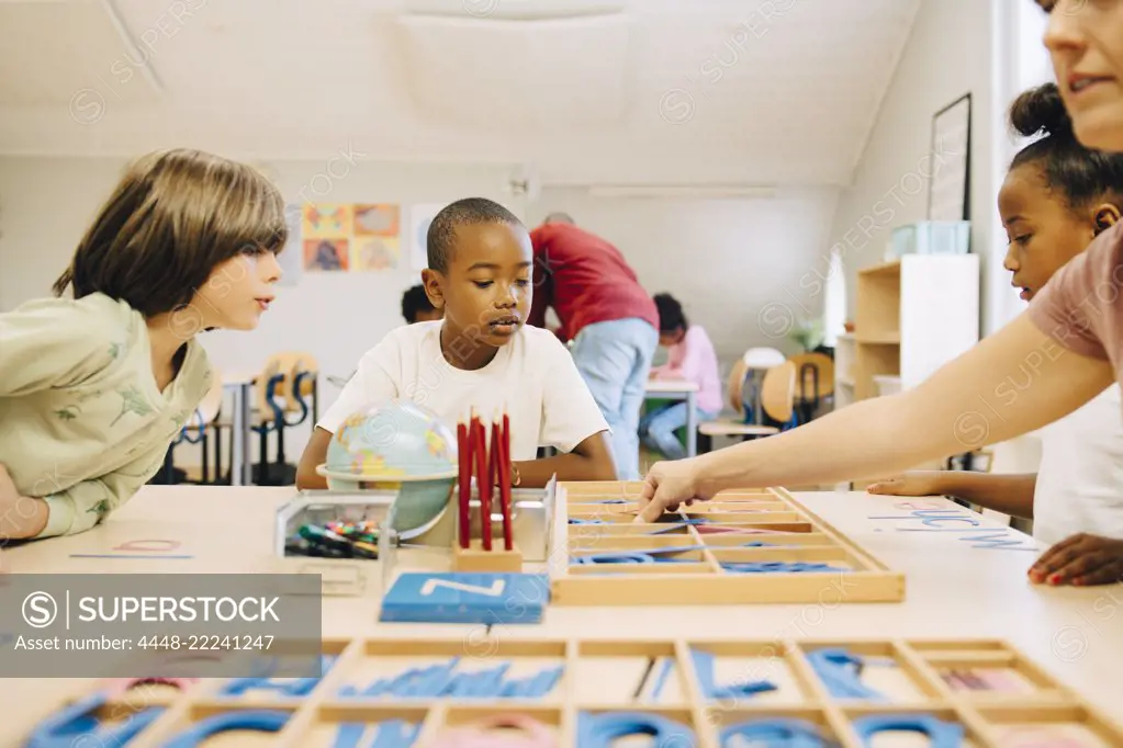 Students learning spellings at table by teacher in classroom