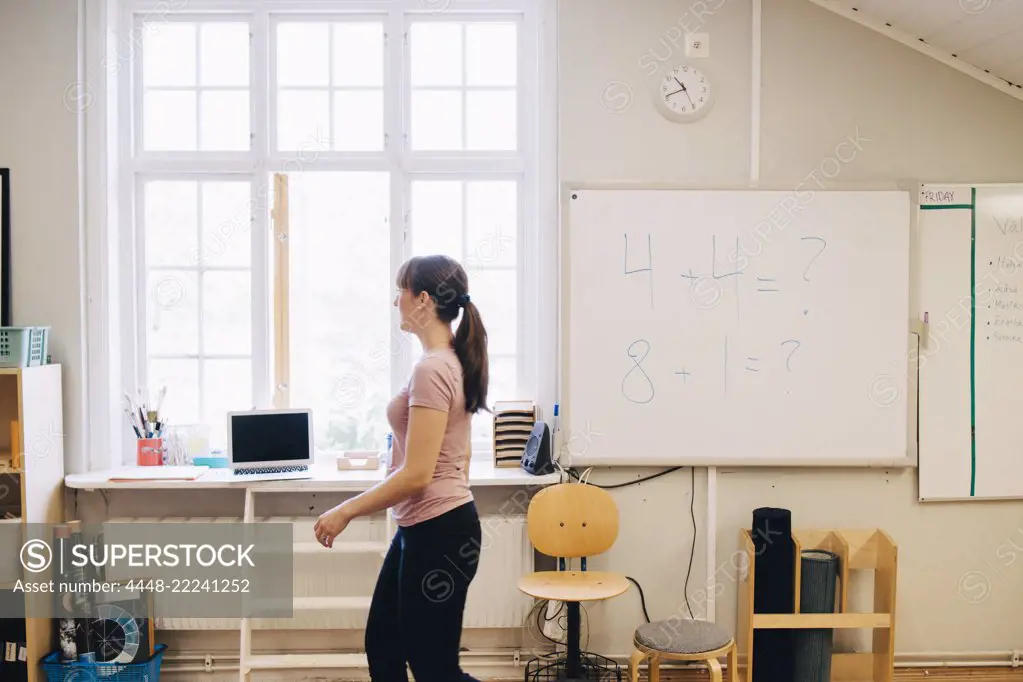 Side view of teacher walking by whiteboard with mathematics in classroom