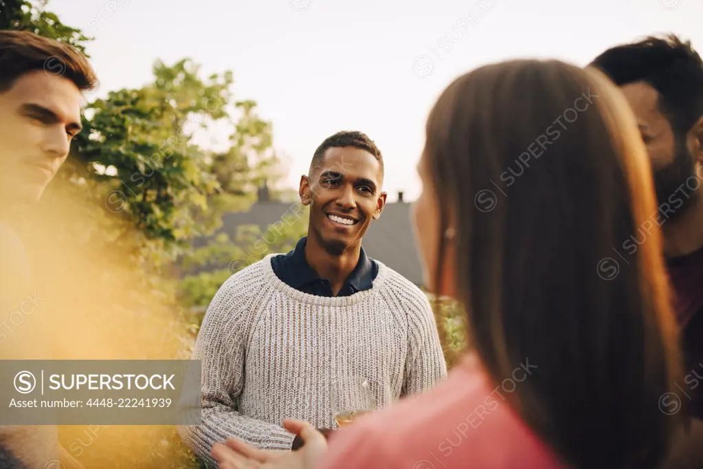 Multi-ethnic friends talking while standing in yard during social gathering