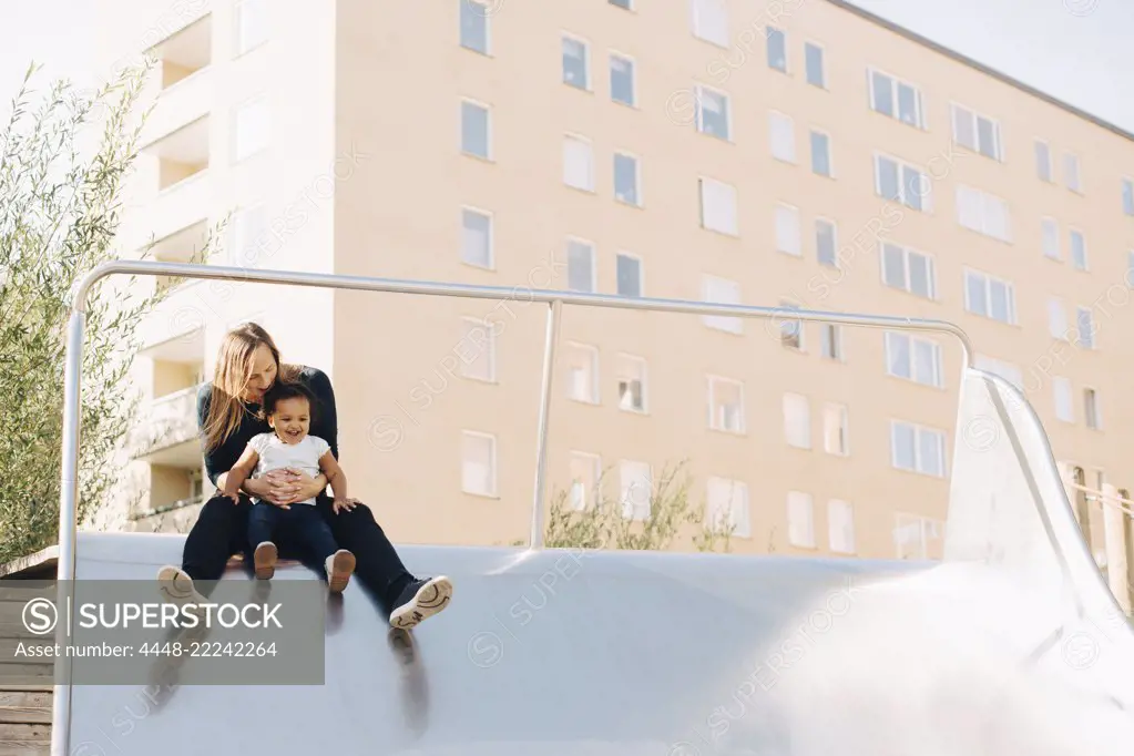 Mother playing with daughter on slide at park in city